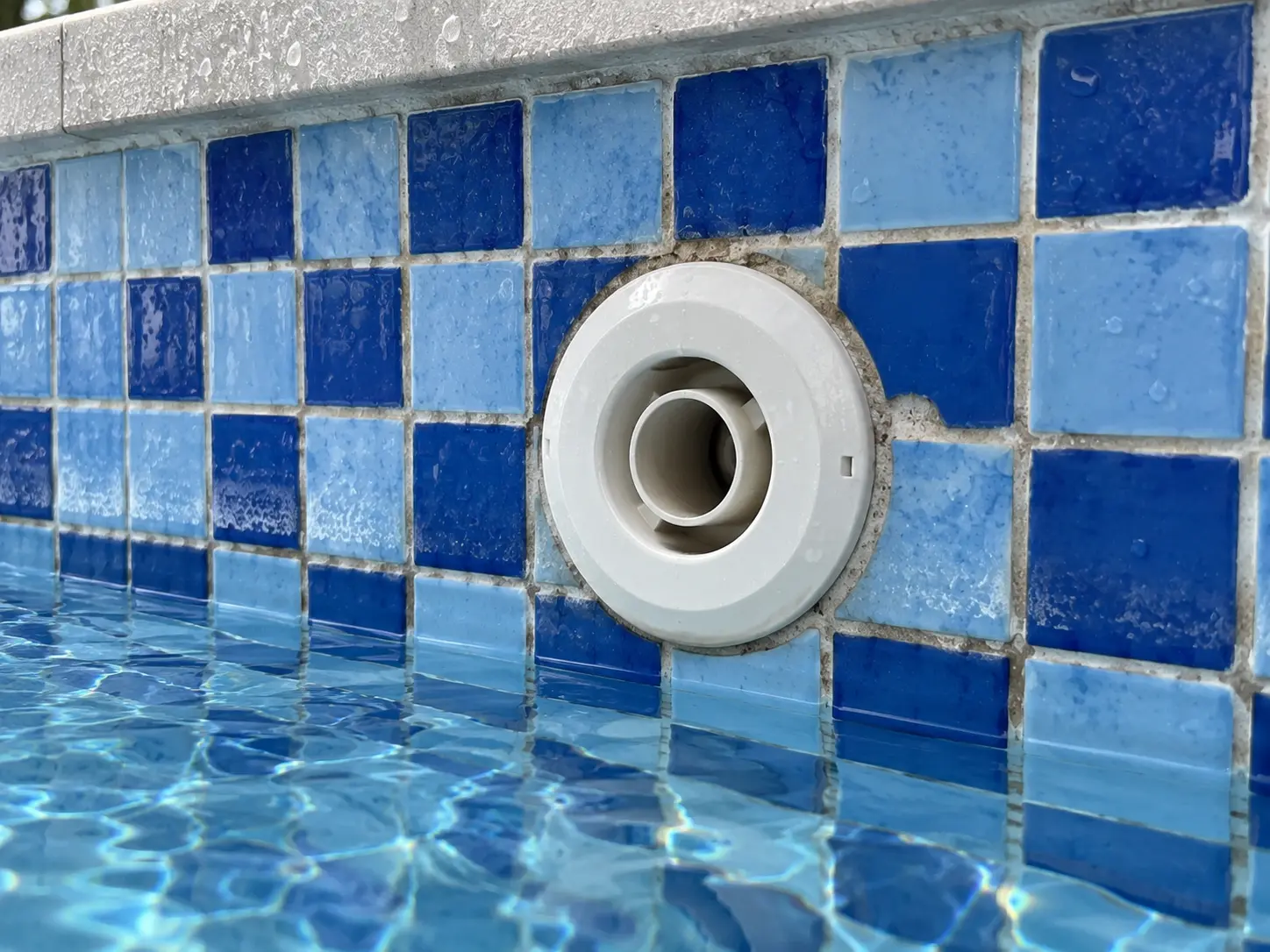 Return inlet fitting in a tiled pool wall, with worn grout around it